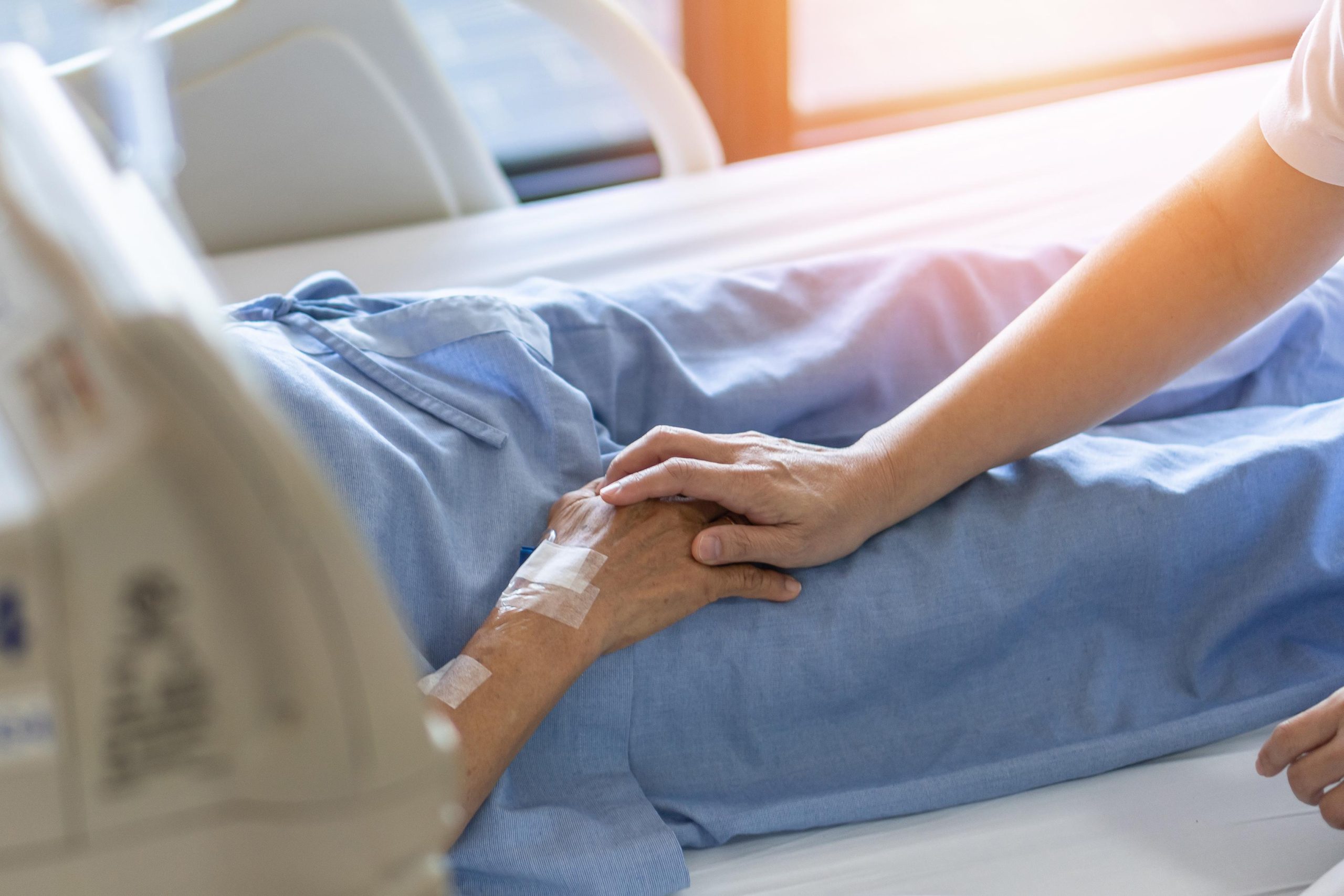 elderly patient lying on bed with nurse gently holding hand